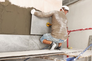 Photo of Worker installing wall tile with vacuum holder indoors, back view