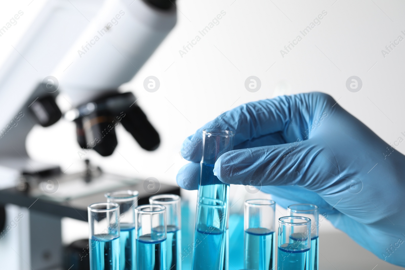 Photo of Scientist taking test tube with light blue liquid in laboratory, closeup