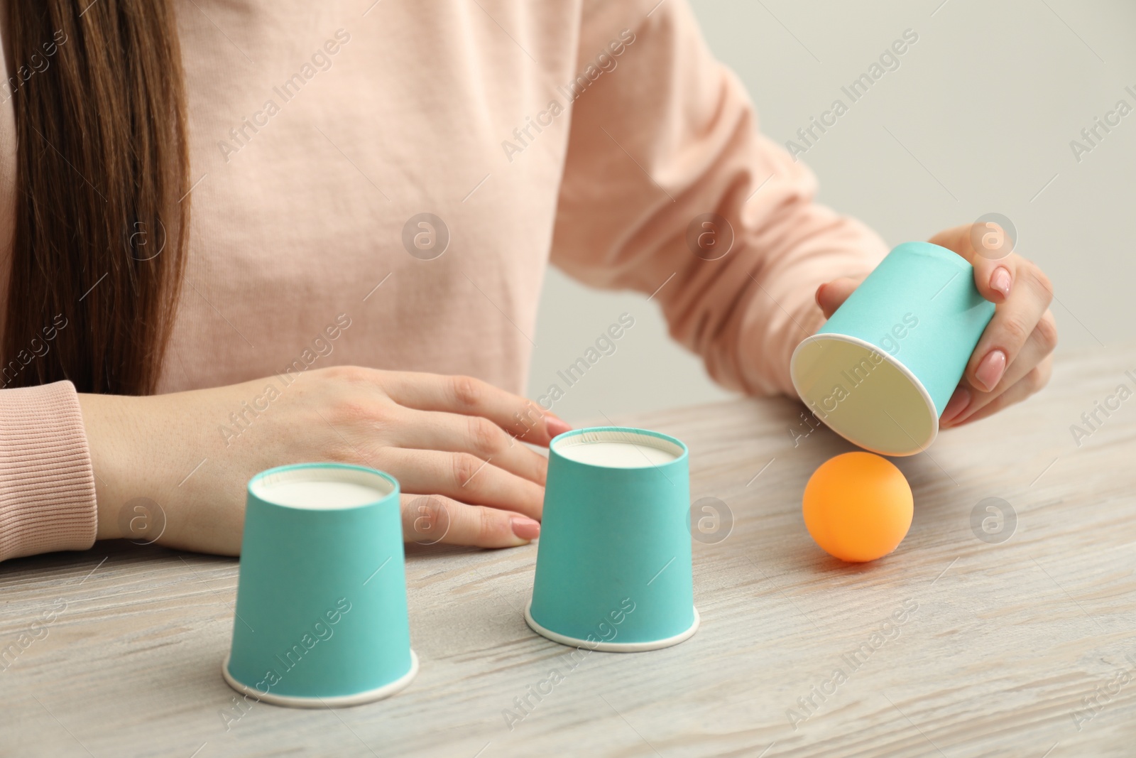 Photo of Shell game. Woman showing ball under cup at wooden table, closeup