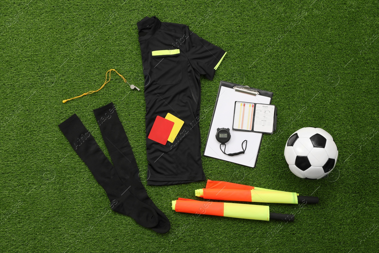 Photo of Uniform, soccer ball and other referee equipment on green grass, flat lay