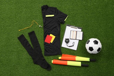 Photo of Uniform, soccer ball and other referee equipment on green grass, flat lay