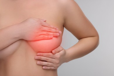 Image of Naked young woman suffering from breast pain on light grey background, closeup