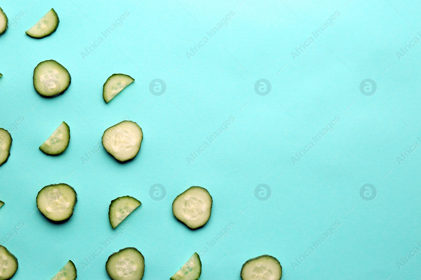 Photo of Slices of fresh ripe cucumber on turquoise background, flat lay. Space for text