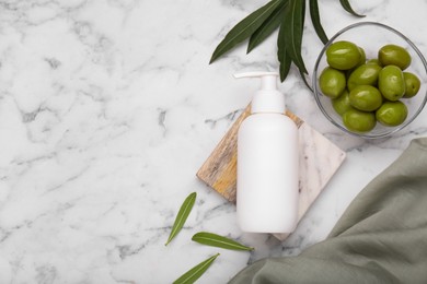 Bottle of cosmetic product with olive essential oil and leaves on white marble table, flat lay. Space for text