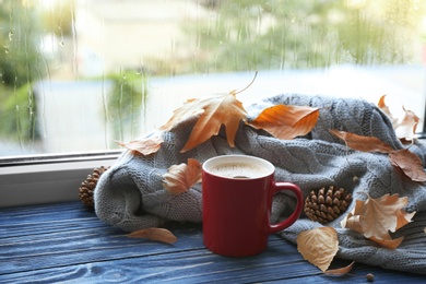 Photo of Cup of hot drink, sweater and autumn leaves on windowsill. Cozy atmosphere