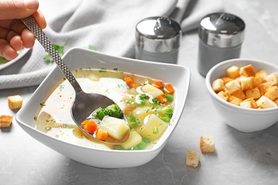 Woman eating fresh homemade vegetable soup at grey marble table, closeup