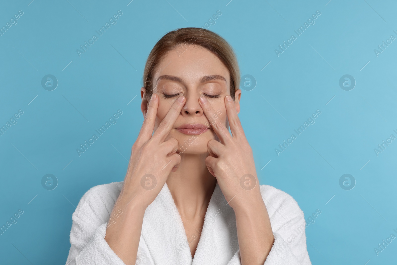 Photo of Woman massaging her face on turquoise background