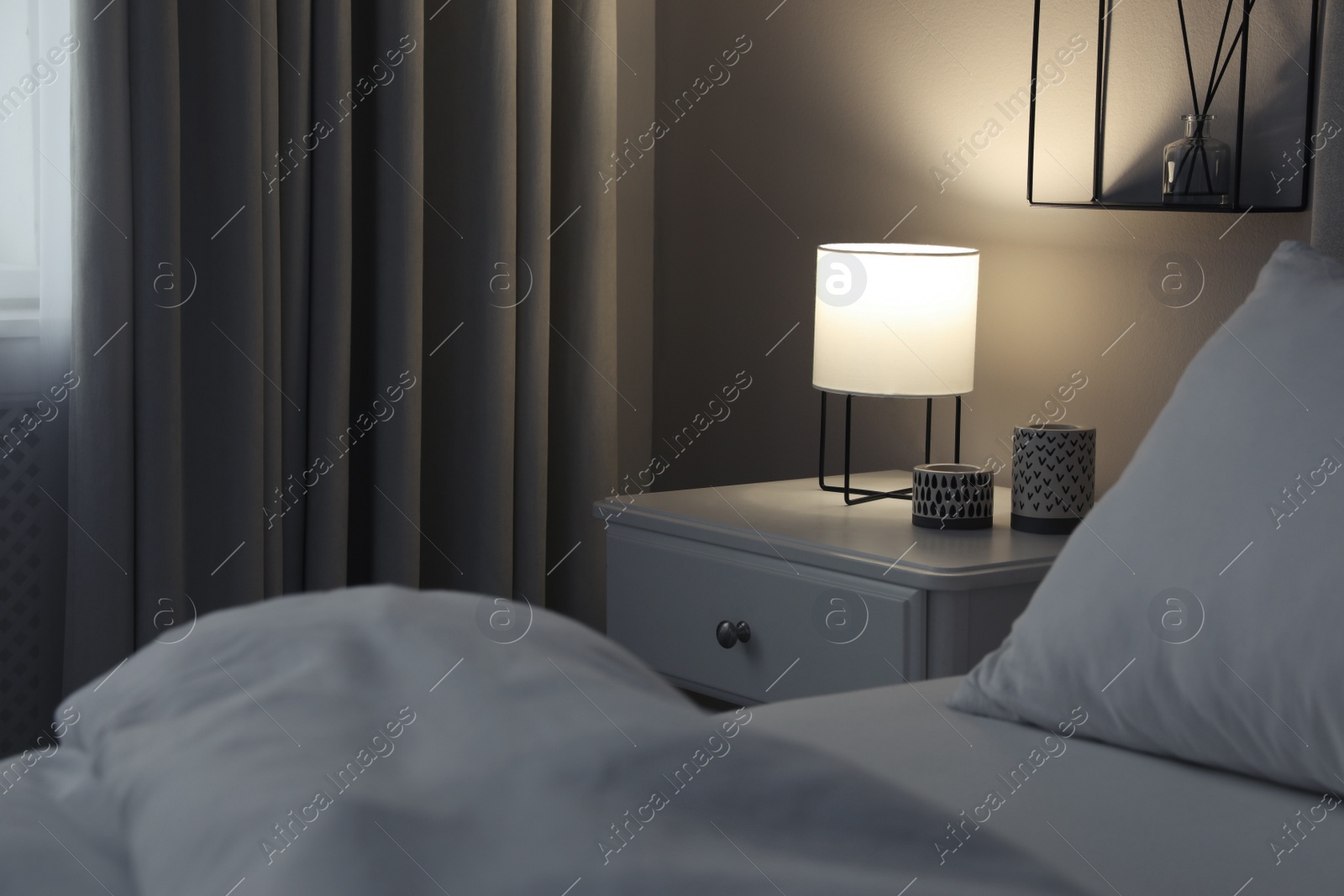 Photo of Stylish lamp and candles on white nightstand in bedroom