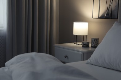 Stylish lamp and candles on white nightstand in bedroom