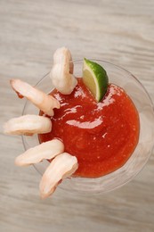 Photo of Tasty shrimp cocktail with sauce and lime in glass on wooden table, top view