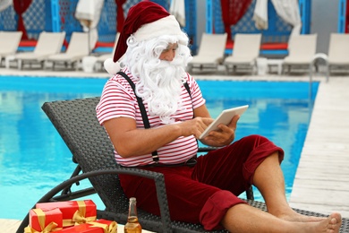 Photo of Authentic Santa Claus with tablet resting on lounge chair at resort