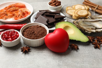 Photo of Natural aphrodisiac. Different food products and heart model on grey table, closeup