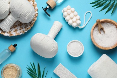 Photo of Beautiful spa composition with herbal massage bags and different care products on light blue background, flat lay