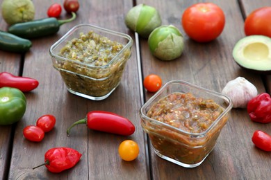Photo of Tasty salsa sauces and ingredients on wooden table