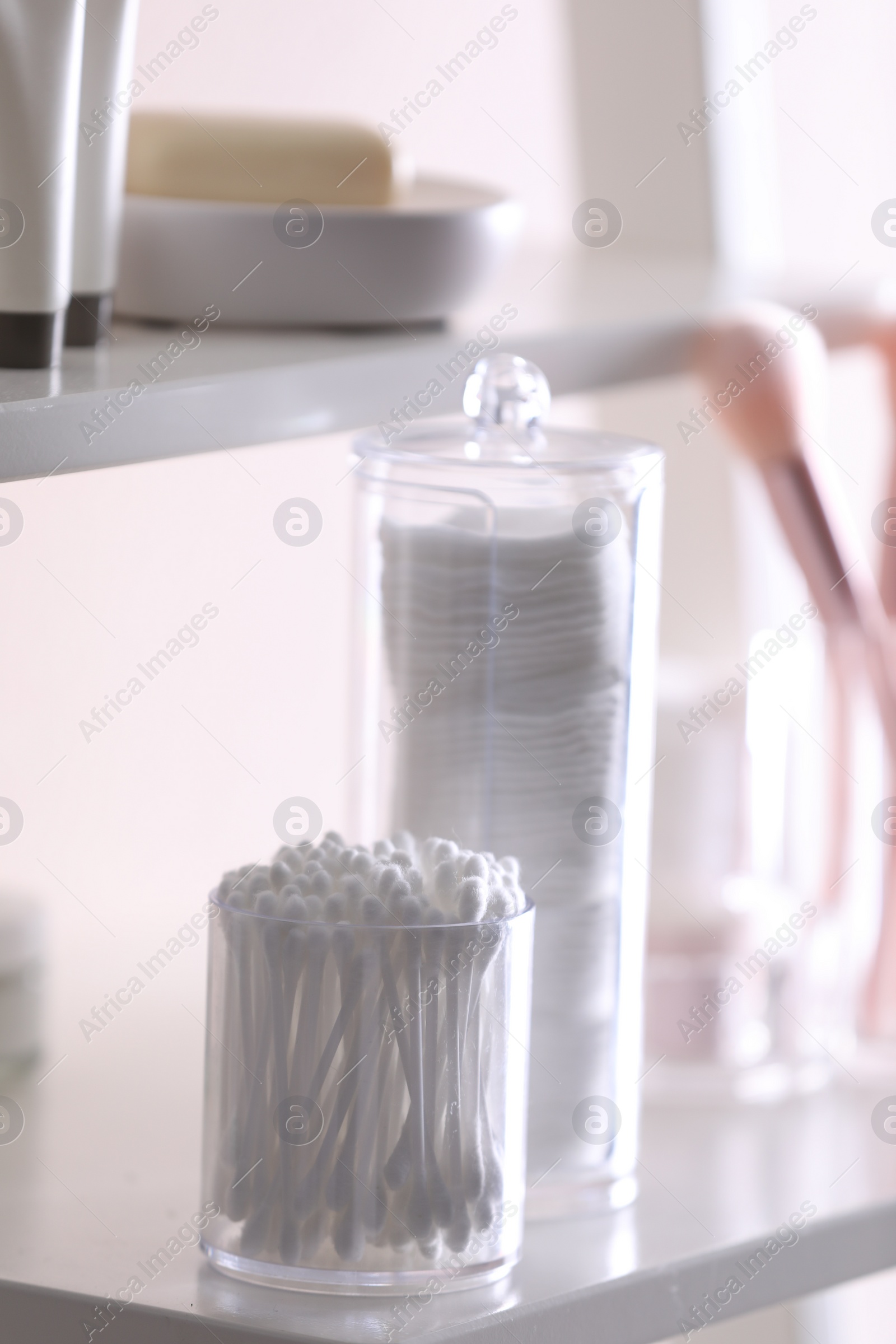 Photo of Cotton buds and pads in transparent holders on shelf