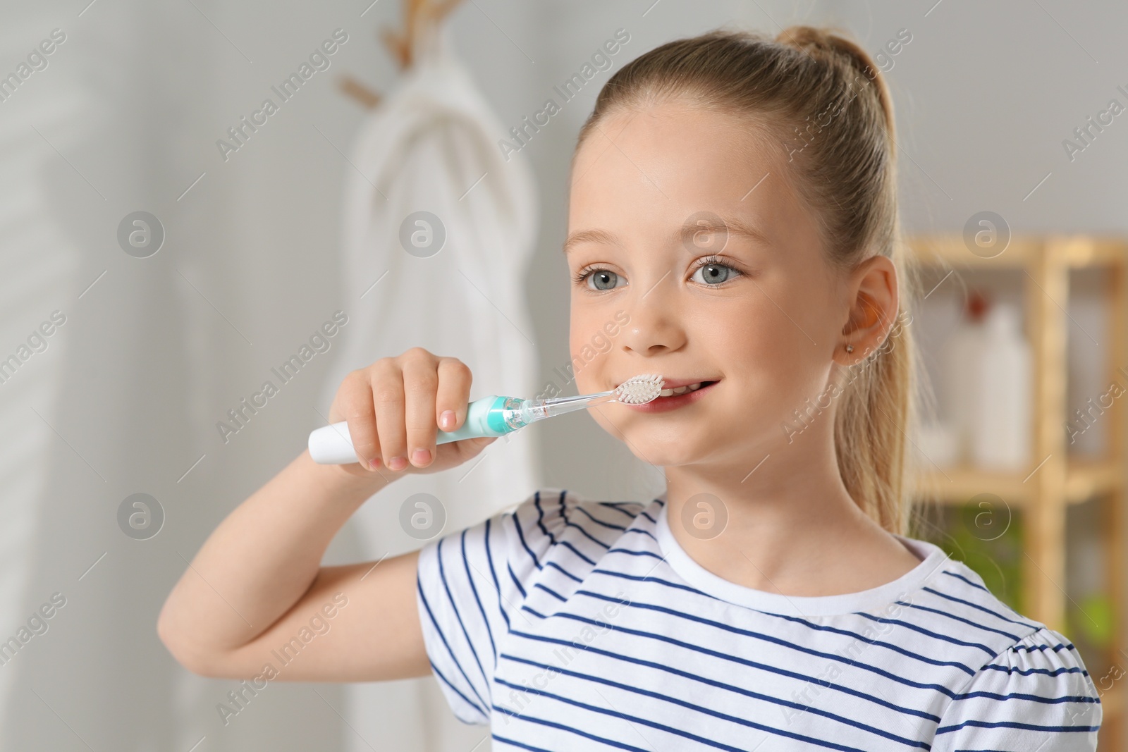 Photo of Cute little girl brushing her teeth with plastic toothbrush in bathroom