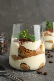 Photo of Delicious tiramisu with mint in glass on grey table