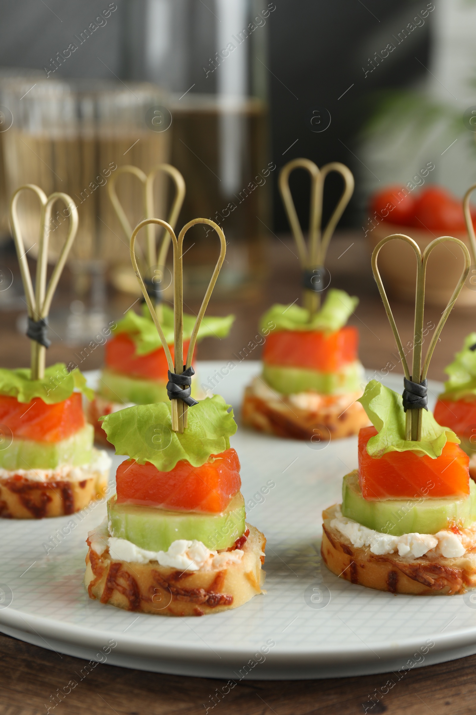 Photo of Tasty canapes with salmon, cucumber, bread and cream cheese on wooden table, closeup