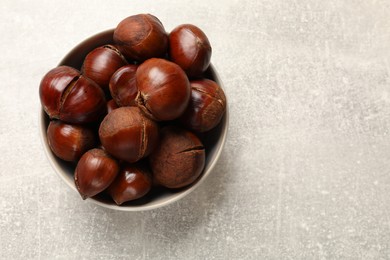 Photo of Fresh edible sweet chestnuts in bowl on grey table, top view. Space for text
