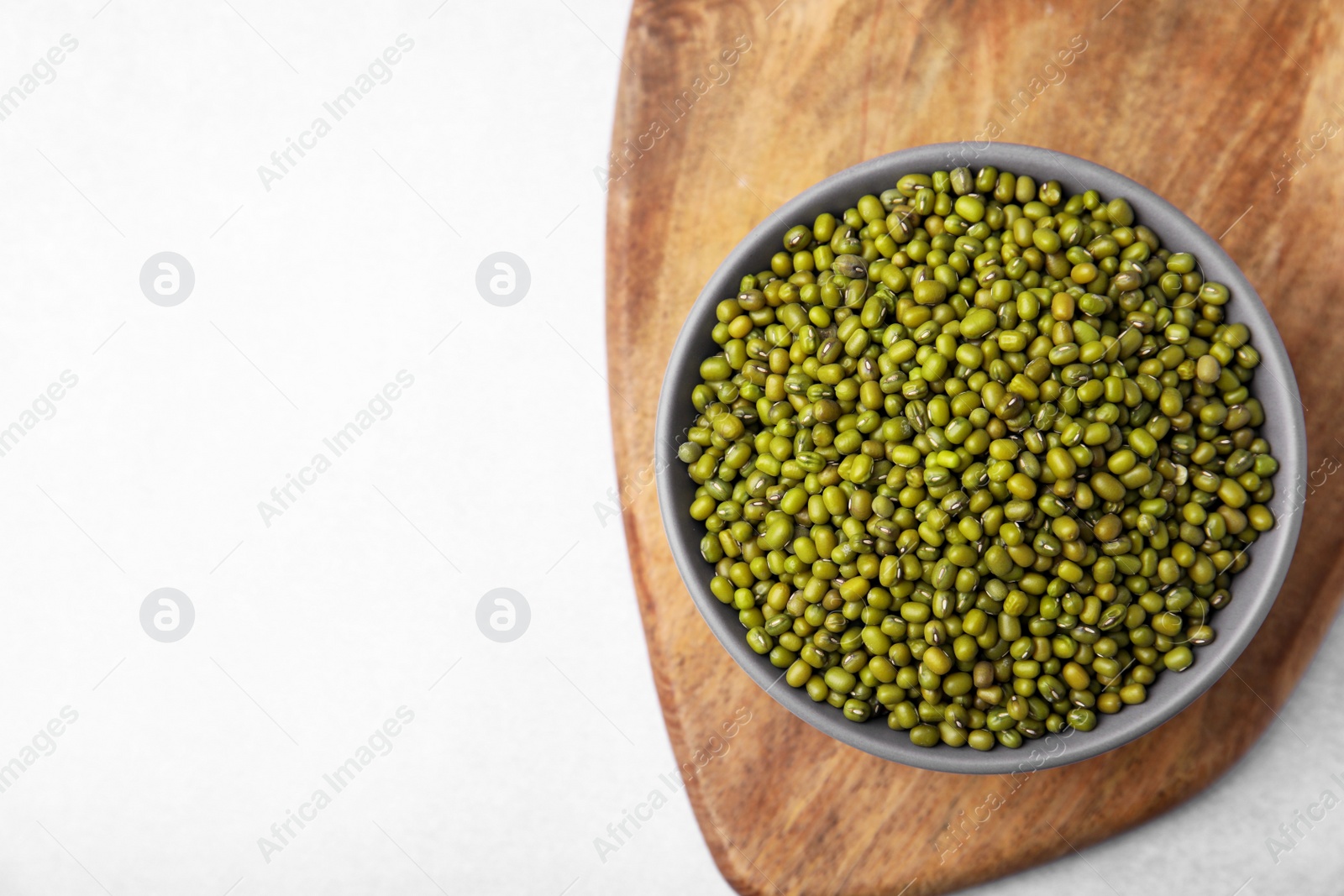 Photo of Bowl with green mung beans and wooden board on white table, top view. Space for text