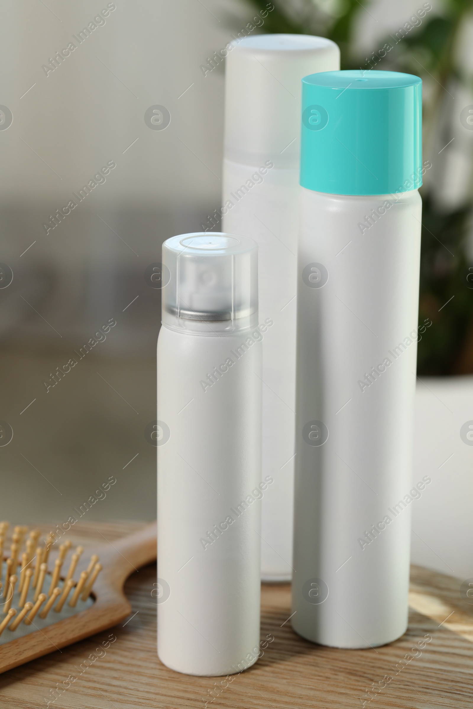 Photo of Bottles of dry shampoos and hairbrush on wooden table indoors