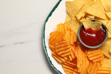 Photo of Plate with tasty ketchup, ridged and tortilla chips on marble table, top view. Space for text