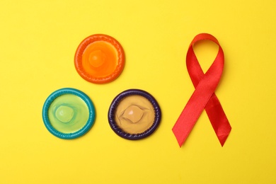 Flat lay composition with colorful condoms and red ribbon on yellow background. LGBT concept