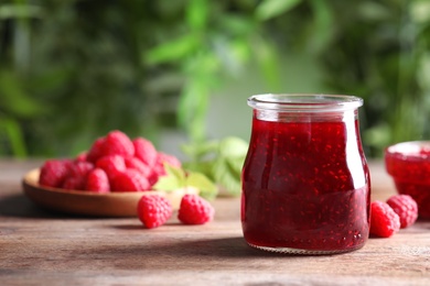 Photo of Glass jar of sweet jam with ripe raspberries on wooden table. Space for text