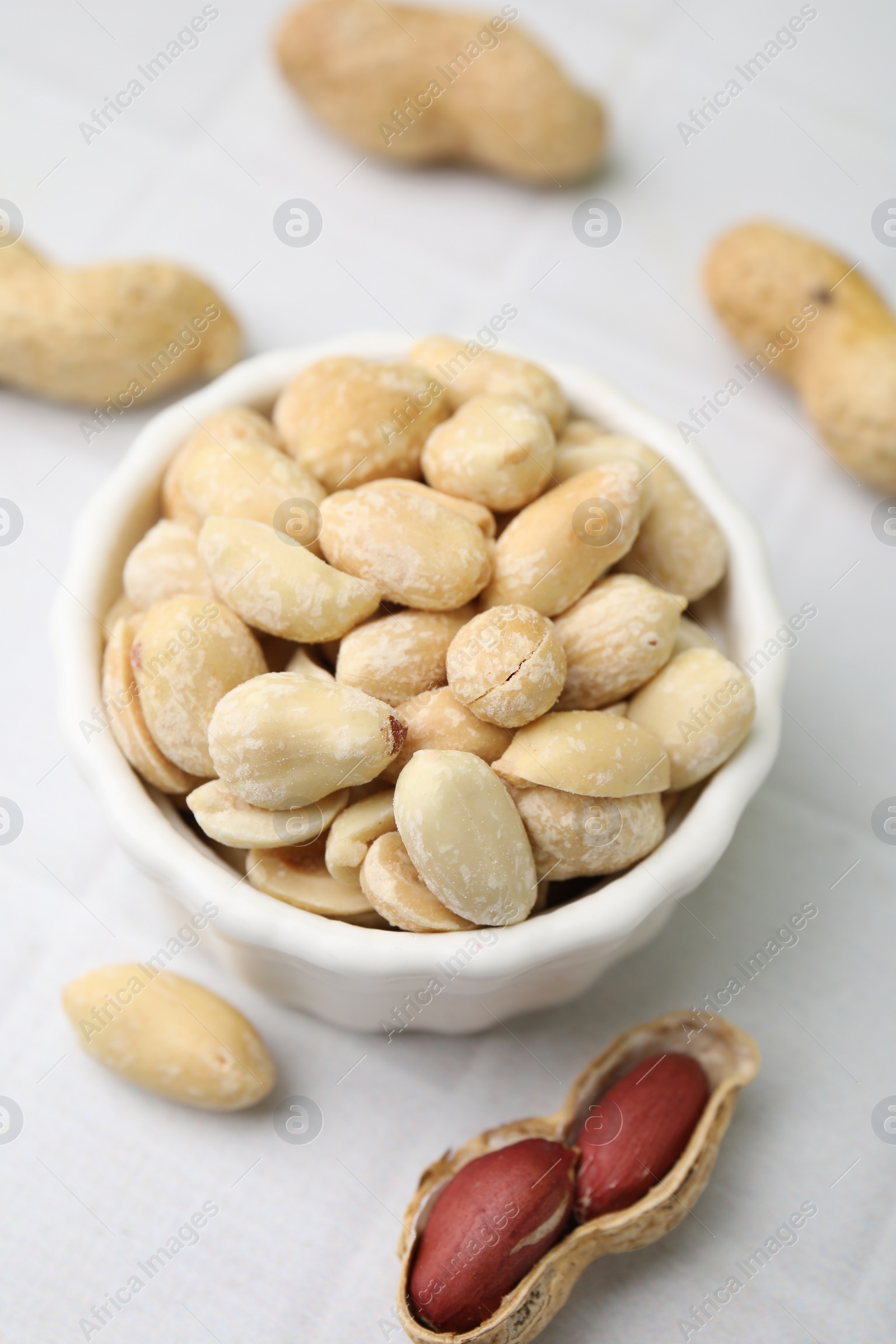 Photo of Fresh peeled peanuts in bowl on white tiled table, closeup