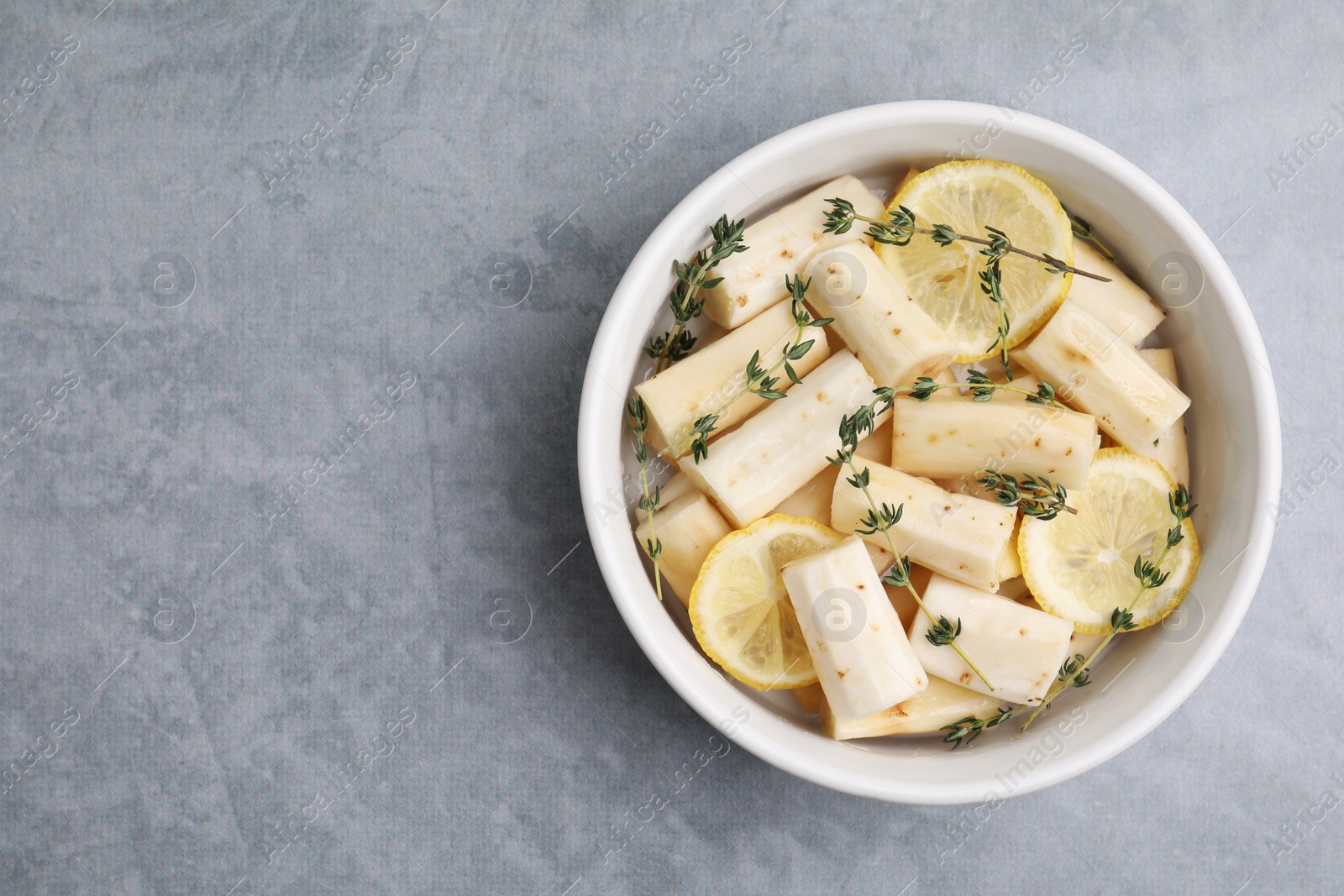 Photo of Dish with raw salsify roots, lemon and thyme on light grey table, top view. Space for text