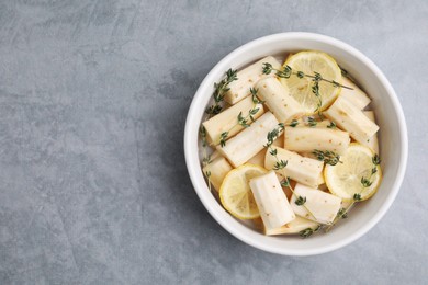 Dish with raw salsify roots, lemon and thyme on light grey table, top view. Space for text