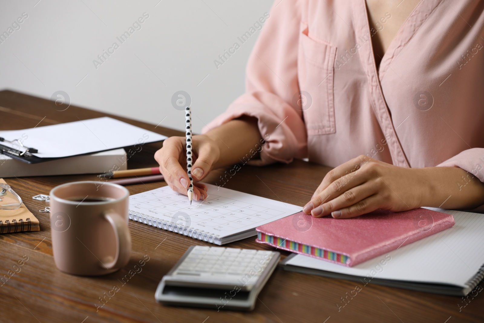 Photo of Woman marking date in calendar at wooden table, closeup