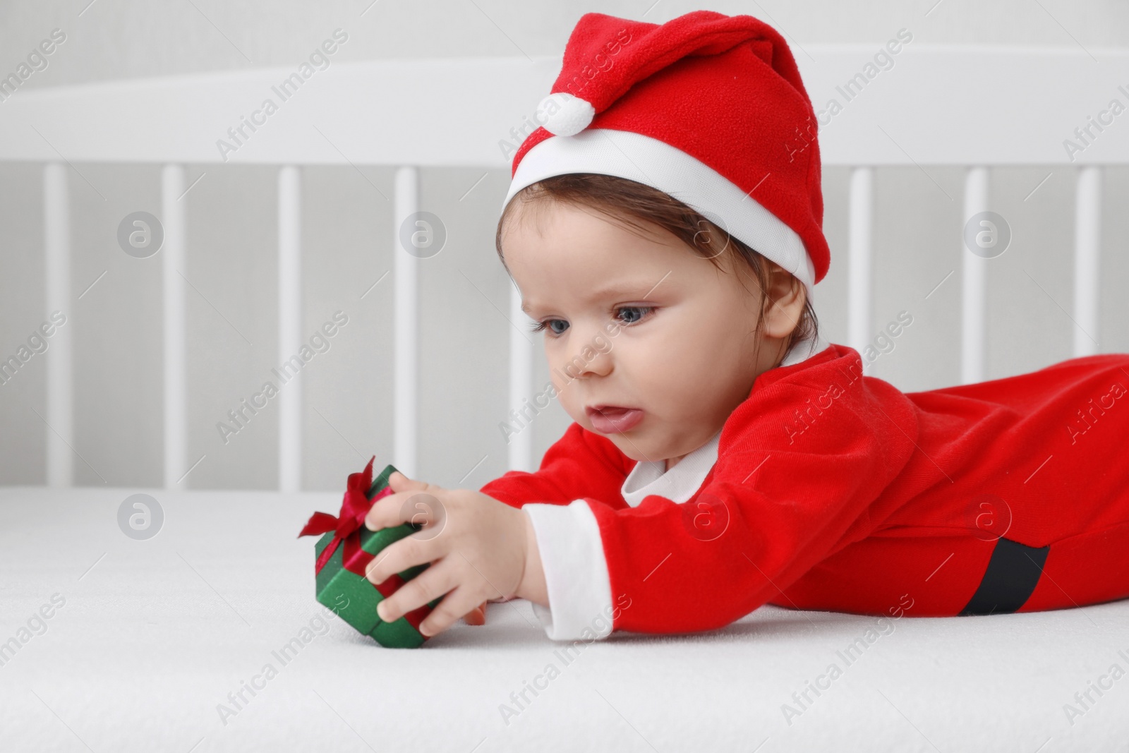 Photo of Cute baby wearing festive Christmas costume with gift box in crib