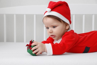 Cute baby wearing festive Christmas costume with gift box in crib