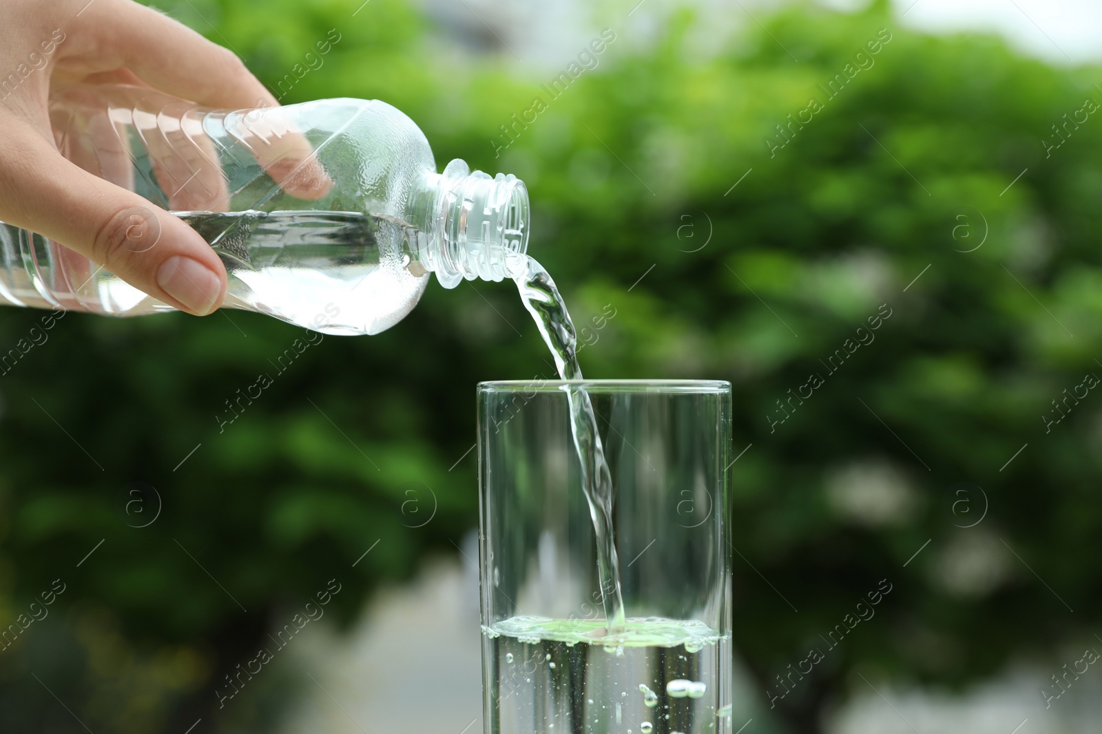 Photo of Woman pouring water from bottle into glass outdoors, closeup