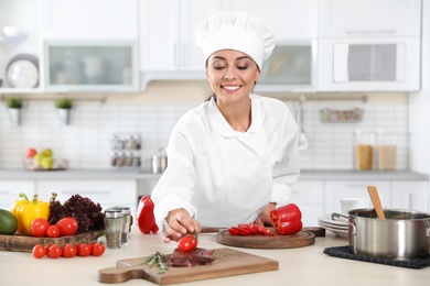 Photo of Professional female chef cooking meat on table in kitchen