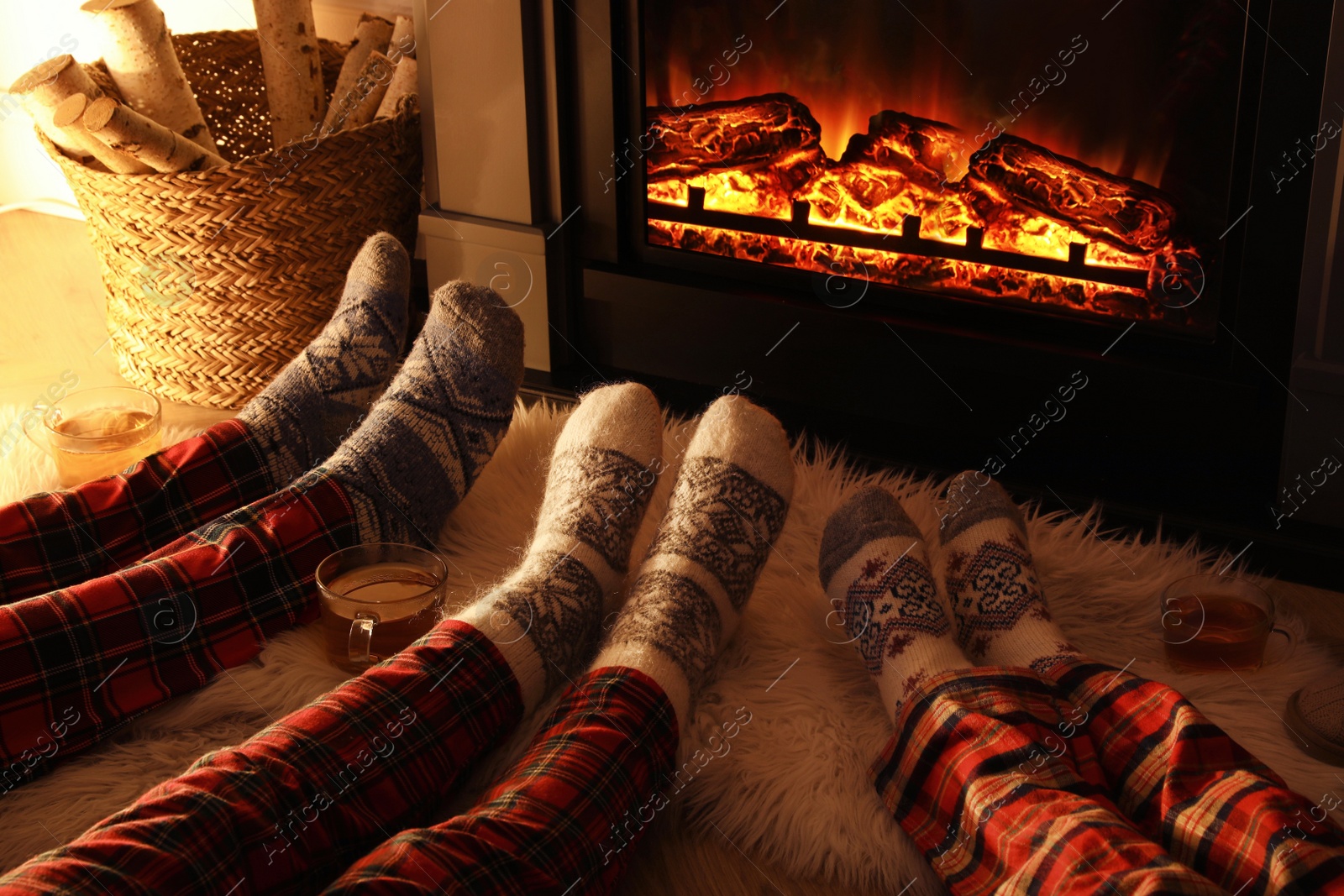 Photo of Family in warm socks resting near fireplace at home, closeup of legs