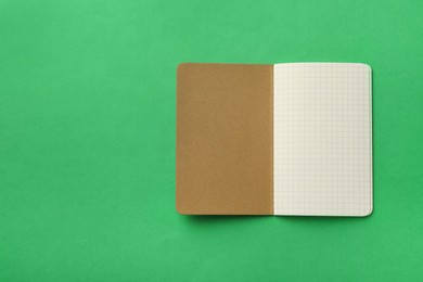 Photo of Stylish open notebook with blank sheets on green background, top view. Space for text