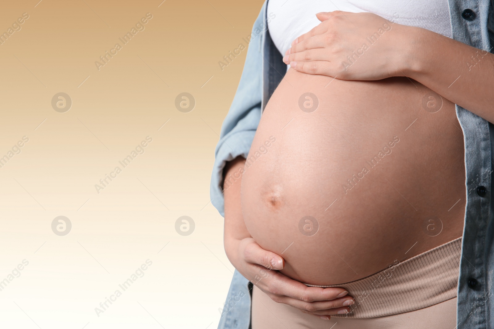 Image of Young pregnant woman touching her belly on beige background, closeup. Space for text