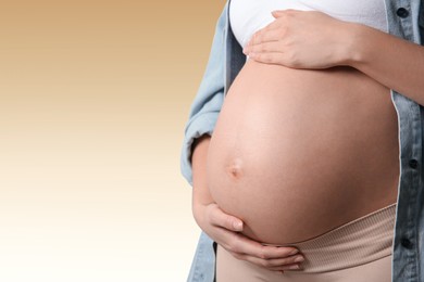 Image of Young pregnant woman touching her belly on beige background, closeup. Space for text