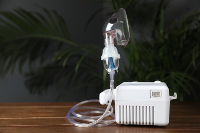 Photo of Modern nebulizer with face mask on wooden table indoors, space for text. Inhalation equipment