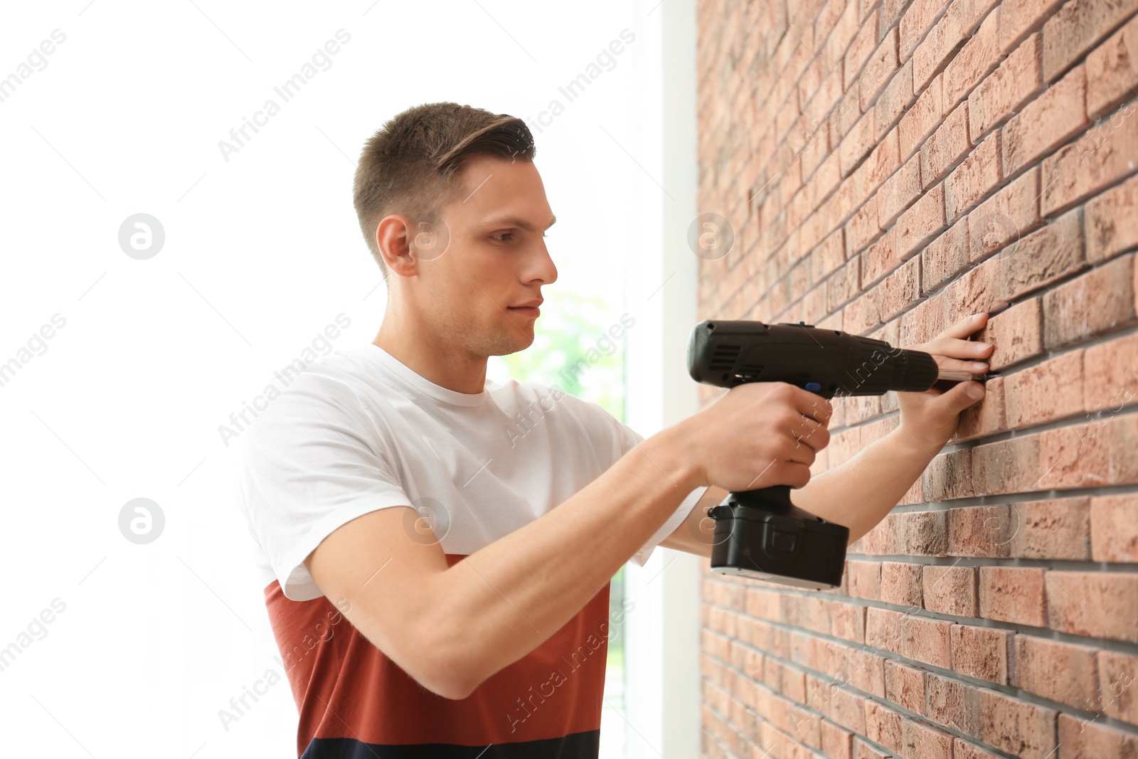 Photo of Young man working with electric screwdriver near brick wall