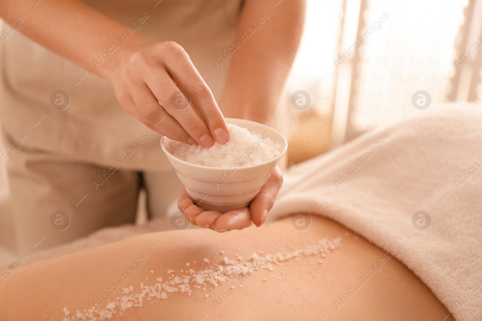 Photo of Young woman having body scrubbing procedure with sea salt in spa salon, closeup