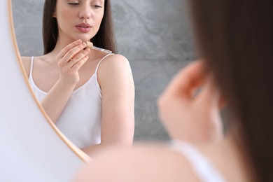 Woman applying essential oil onto shoulder near mirror, closeup