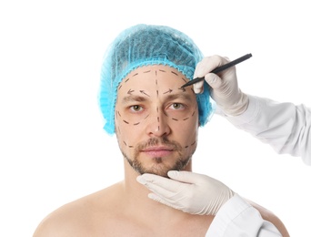 Photo of Doctor drawing marks on man's face for cosmetic surgery operation against white background