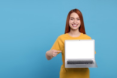 Smiling young woman showing laptop on light blue background, space for text