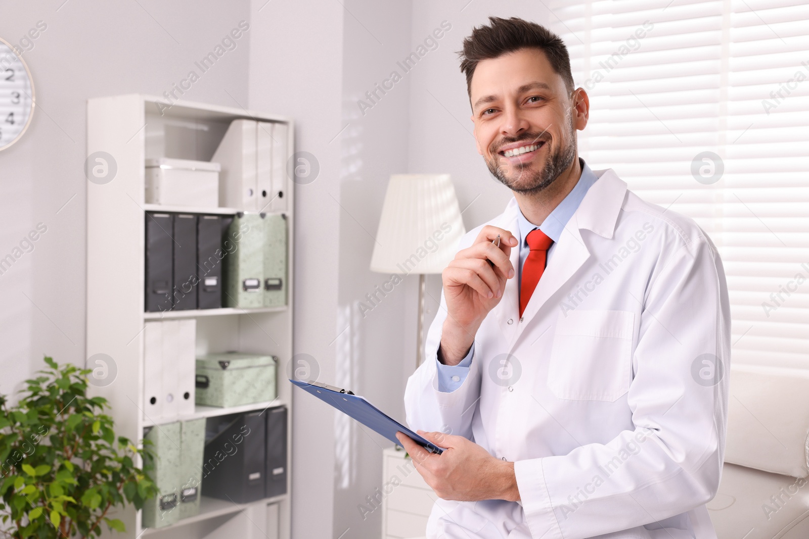 Photo of Happy doctor with clipboard in clinic, space for text. Patient consultation