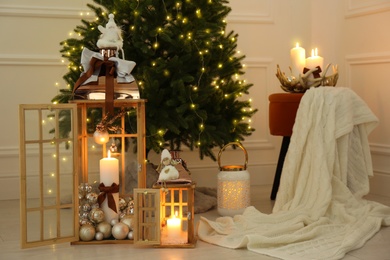 Wooden decorative lanterns with burning candles near Christmas tree indoors