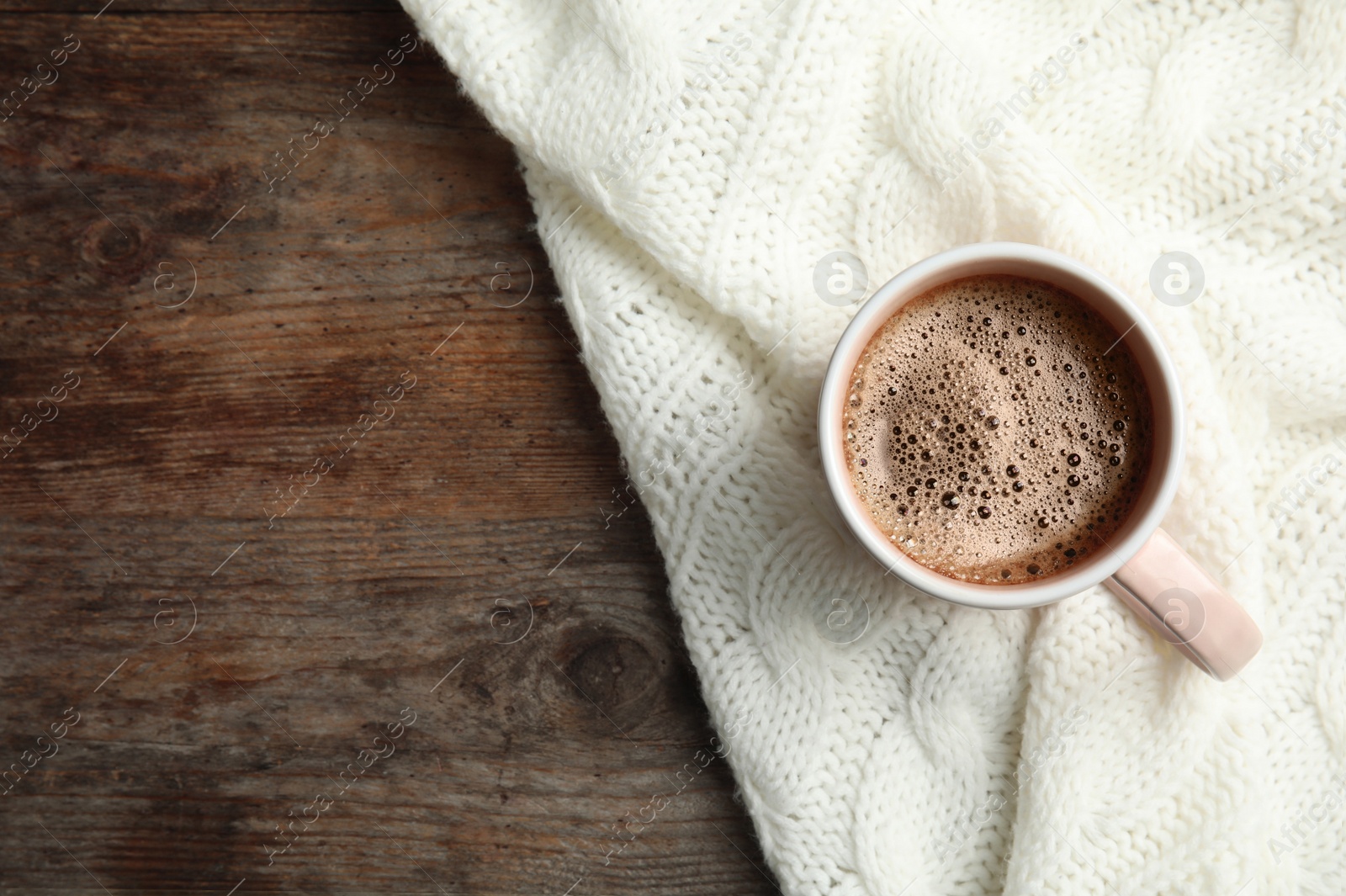 Photo of Cup of hot winter drink and knitted plaid on wooden background, top view with space for text. Cozy season