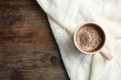 Cup of hot winter drink and knitted plaid on wooden background, top view with space for text. Cozy season